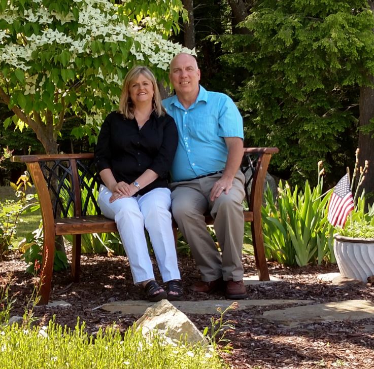 A couple sitting on a wooden bench in a garden surrounded by greenery.